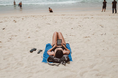 Woman using digital tablet while lying at sandy beach