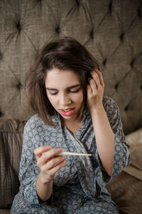 Woman checking thermometer while sitting on bed