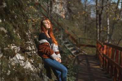 Woman with closed eyes standing by rock outdoors