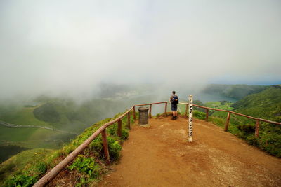 Man standing on railing against sky