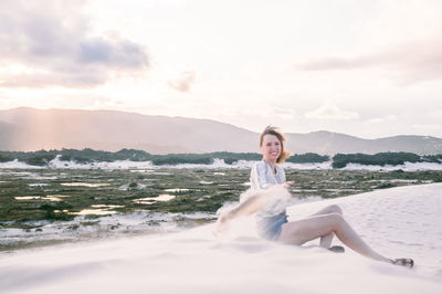 Portrait of young woman sitting on beach against sky