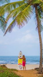 Woman standing by palm tree on beach against sky