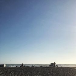 People on beach against clear blue sky