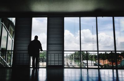 Rear view of silhouette man looking through window