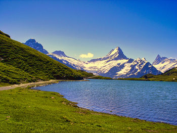 Scenic view of lake and mountains against clear blue sky