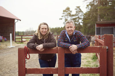 Mature couple leaning on fence in farm