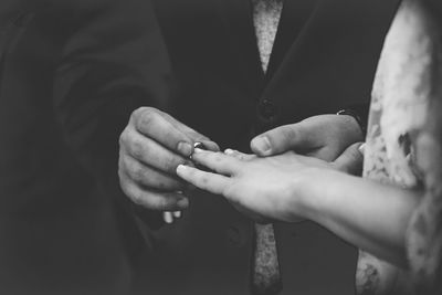 Midsection of groom exchanging ring with bride during wedding