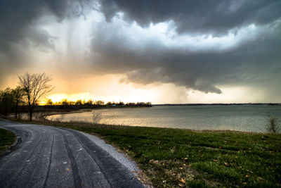 Road passing through field against cloudy sky