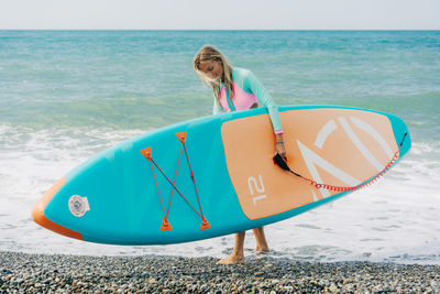 Happy smiling young woman carries sup board into the sea.