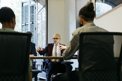 Businessman gesturing while discussing with colleagues at table in office