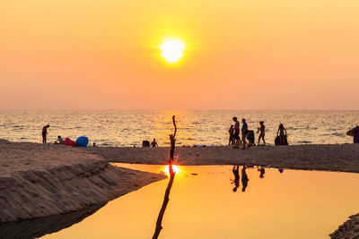 Silhouette people on beach against sky during sunset