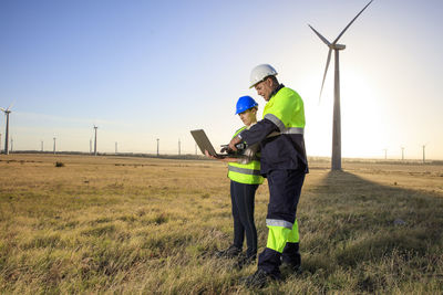 Two engineers with laptop discussing on a wind farm