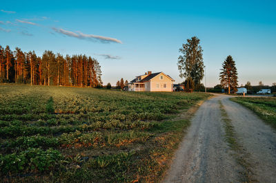 Road amidst field and houses against sky