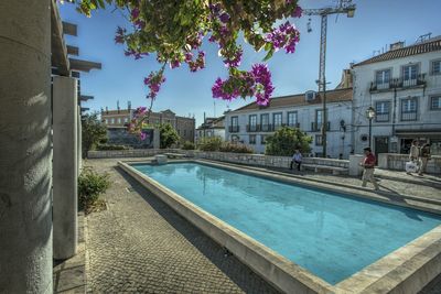 Swimming pool by buildings in city against sky