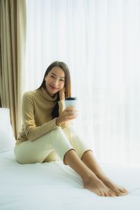 Young woman using phone while sitting on bed