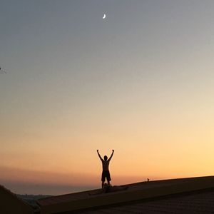 Silhouette man with arms outstretched standing at sunset