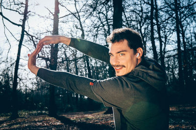 Runner is doing stretching in the woods. man with blue eyes and mustache is training in the park.