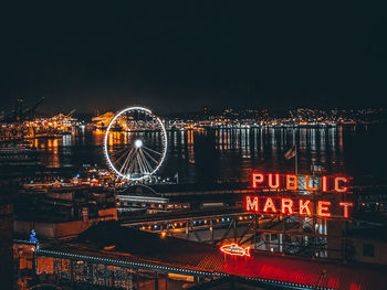 Illuminated ferris wheel in city against sky at night