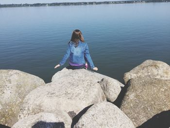 Rear view of woman sitting on rock by sea