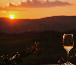 Close-up of wineglass against sky during sunset