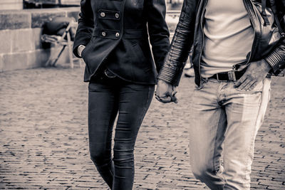 Midsection of couple holding hands white walking on footpath