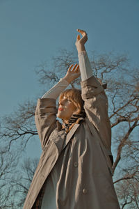 Low angle view of woman standing by bare tree against sky