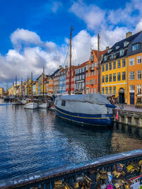 Sailboats moored on river by buildings in city against sky