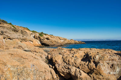 Scenic view of rocky beach against clear blue sky