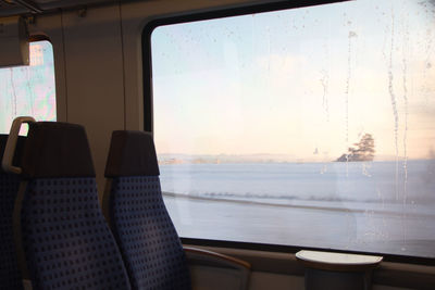 Empty chairs and table against sky seen through glass window