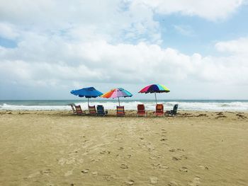 Empty chairs with umbrellas at beach against cloudy sky