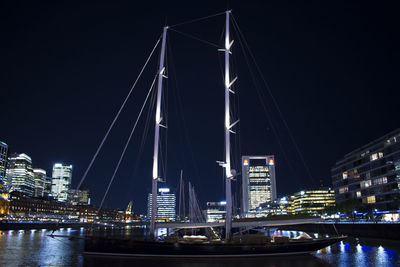 Illuminated bridge over river by buildings against sky at night