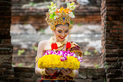 Smiling young woman in traditional clothing holding flowers at temple
