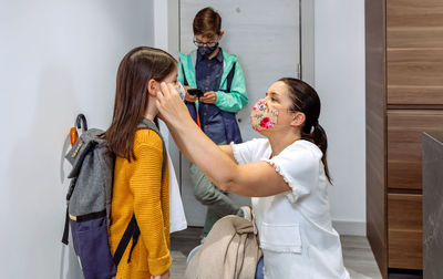 Mother wearing mask to daughter while standing at home