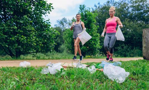 Female friends running towards garbage at park