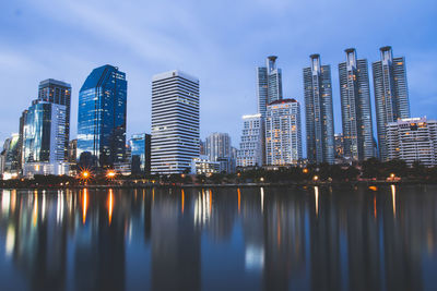 Illuminated buildings by river against sky in city