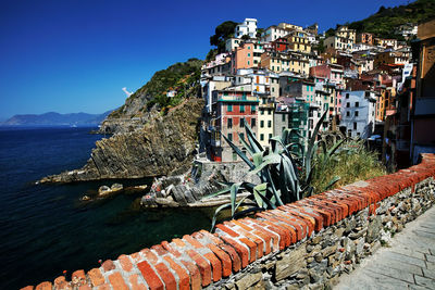 Residential buildings by sea against clear blue sky