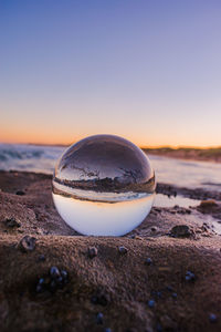 Close-up of crystal ball on beach against sky during sunset