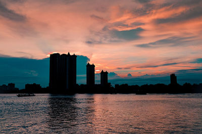 Scenic view of river by buildings against sky during sunset