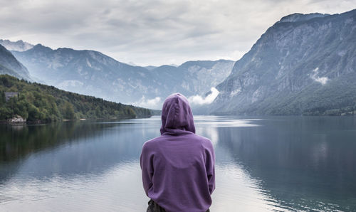 Rear view of man looking at lake against mountain range