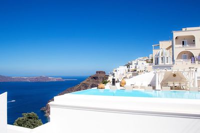 Infinity pool and buildings by sea against clear blue sky