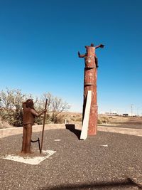 Statue of man standing by sculpture against clear blue sky