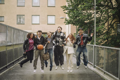 Cheerful teenage friends jumping together on footpath