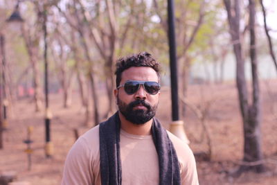 Portrait of young man wearing sunglasses standing against trees