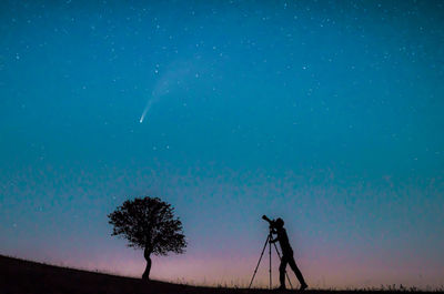 Silhouette man photographing on field against sky at night