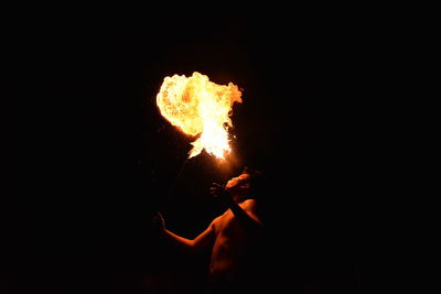 Silhouette man holding fire against black background