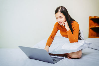 Young woman using phone while sitting on bed