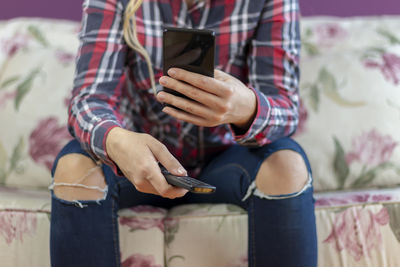 Attractive casual woman using smart phone and holding remote control in her hand. 