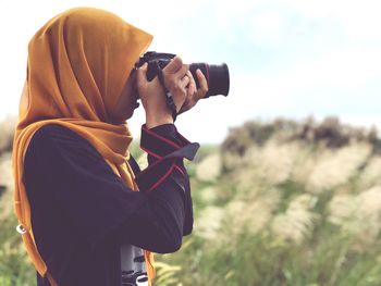 Side view of woman photographing while standing on field