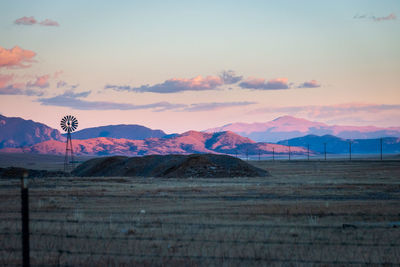 Wind turbines on land against pikes peak and sky during sunset