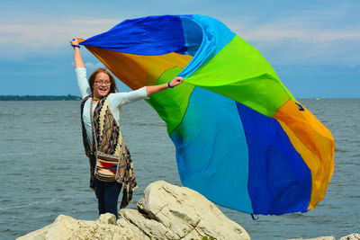 Girl holding fabric while standing at beach against sky